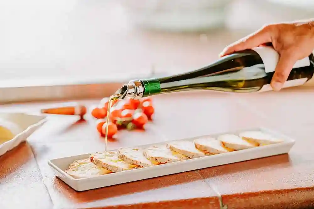 Olive oil being poured over sliced bread on a ceramic plate
