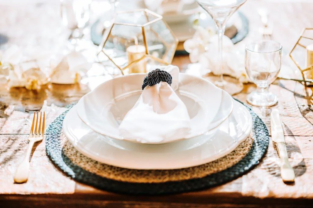 Elegant table setting with white plates, folded napkin, and glassware on a rustic wooden table