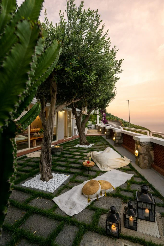 Seafront garden terrace with olive tree, hanging lanterns and sea view, styled for a luxury outdoor relaxation area in Positano.