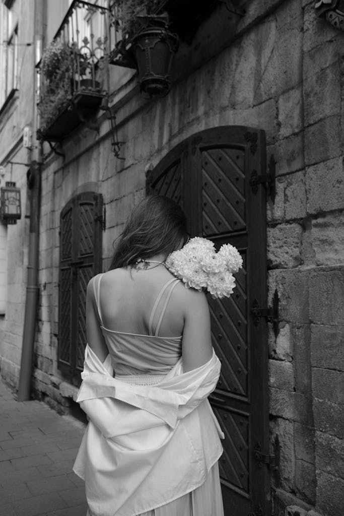 Black and white photo of a woman holding flowers on a cobblestone street.